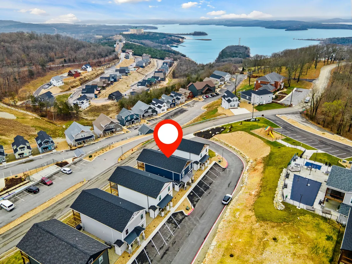 A scenic exterior view featuring newly constructed homes overlooking a picturesque lake and surrounded by rolling hills. The winding road leads through the community, offering panoramic vistas and an inviting sense of space and openness.