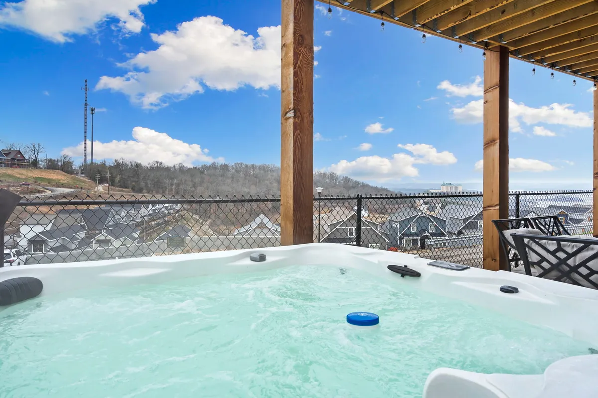This exterior image features a luxurious hot tub nestled underneath a wooden structure, with an expansive view of the surrounding mountain landscape. The setting appears tranquil and private, perfect for unwinding while enjoying the natural scenery. The area is inviting, with enough space for small groups to relax together.