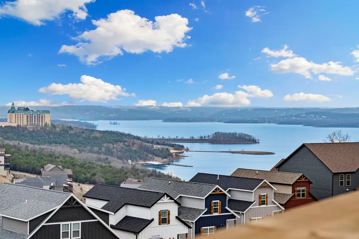 A sweeping view of the lake with distant hills and clouds, framed by lakeside houses. The tranquil scene emphasizes natural beauty and the outdoor recreational opportunities available in the area.