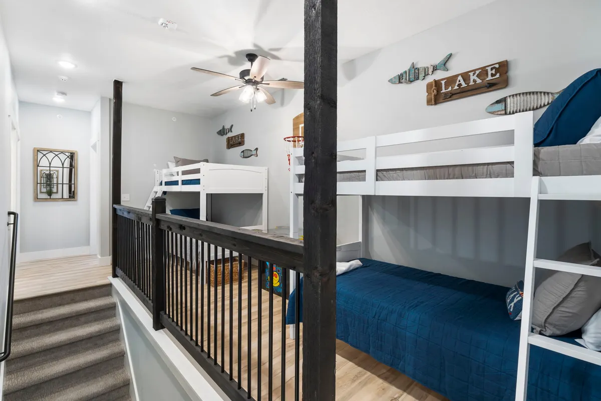 A bright, cheerful bunk room with twin-over-twin beds, blue bedding, lake-themed decor, and a ceiling fan. The space looks inviting for kids, with details that suggest storytelling and playful interaction among young guests.