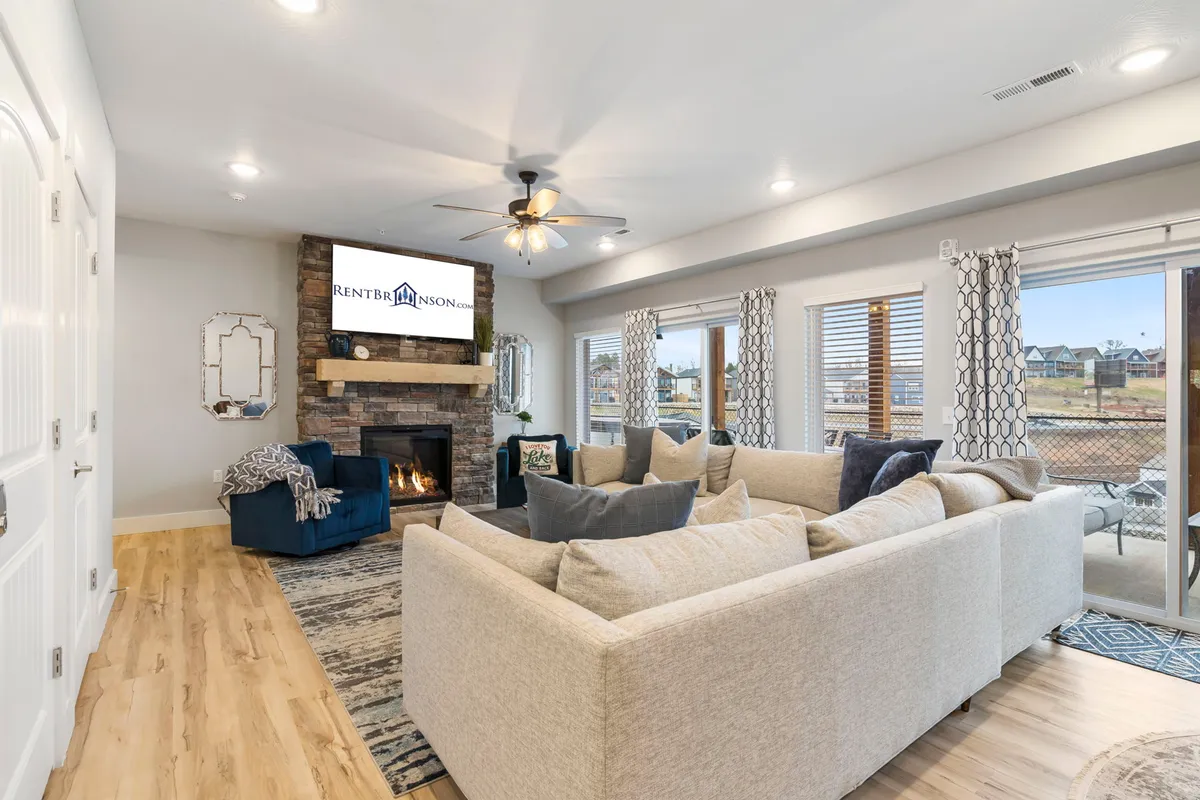 A cozy living lounge with a large sectional sofa, a fireplace, a wall-mounted TV, and expansive windows framing serene views of the outdoors. The arrangement invites both relaxation and group activities, from movie nights to casual conversations.