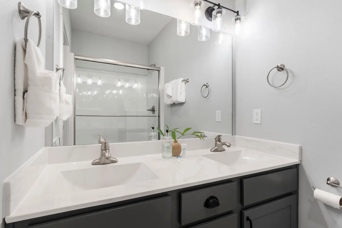 A bright, spa-inspired bathroom featuring a double sink, modern mirrored wall, and elegant light fixtures. The fresh and inviting atmosphere promises a pampering, restorative experience.