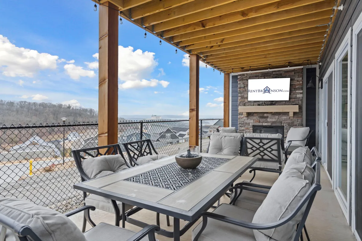 The hero image showcases a spacious outdoor living area with a large dining table, comfortable seating, a cozy stone fireplace, and a mounted television. The setup invites gatherings, relaxation, and enjoying meals together while overlooking scenic lake views. The space is perfect for stargazing, grilling, and celebrating special moments with friends and family in a welcoming, open-air environment.