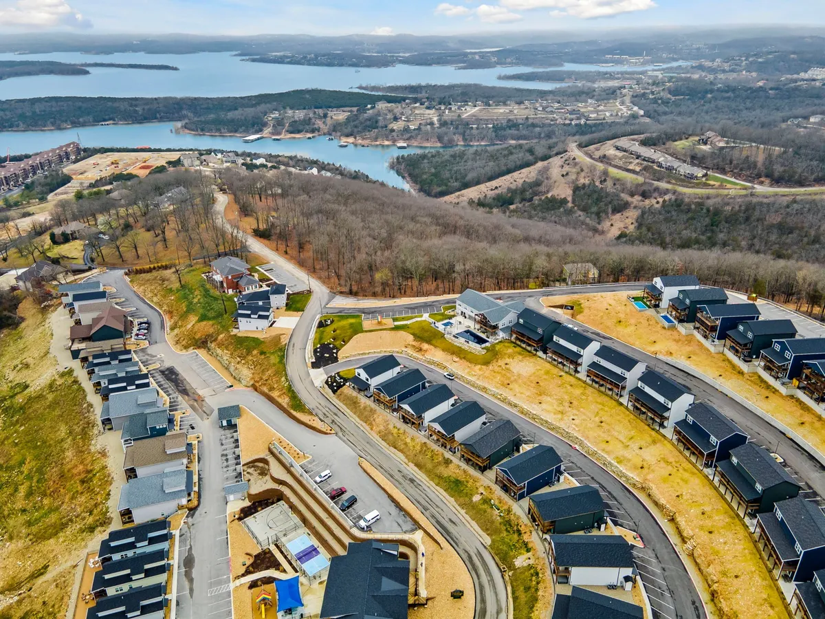 This exterior image showcases newly constructed homes along a winding road, with a beautiful lake in the background and trees surrounding the area. The scene exudes a sense of peaceful community living nestled in scenic nature.